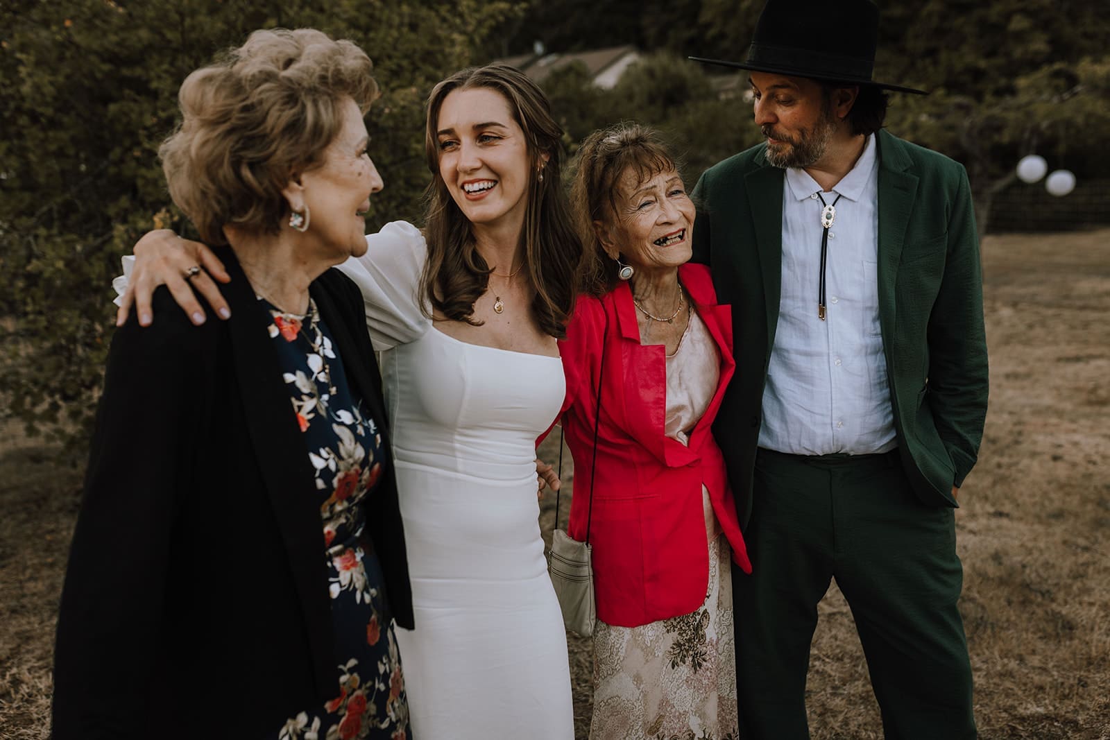 Bride and groom pose for a photo with their grandmas, smiling at each other and laughing 