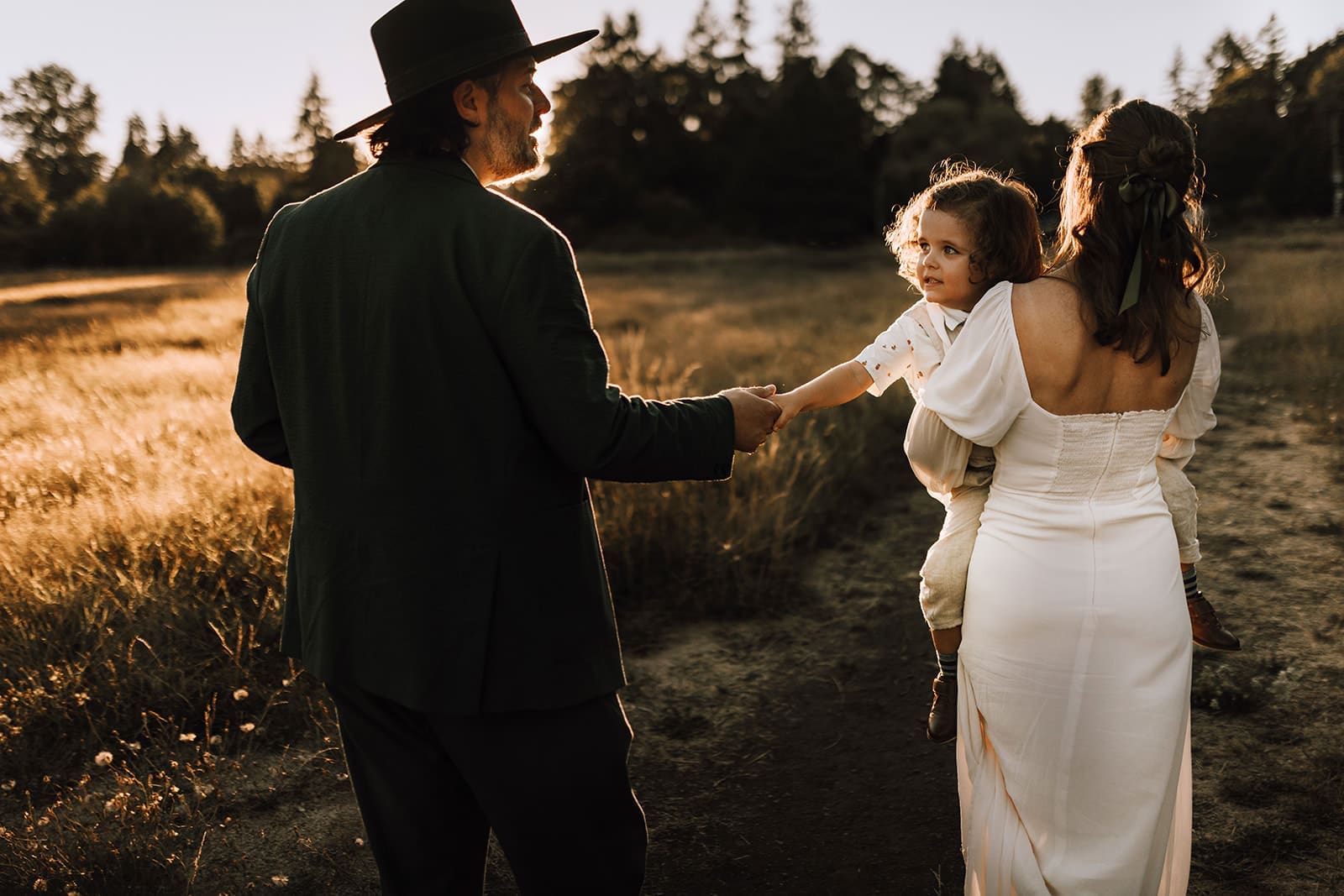Mom, dad, and son having three wedding photo taken during golden hour in a field 