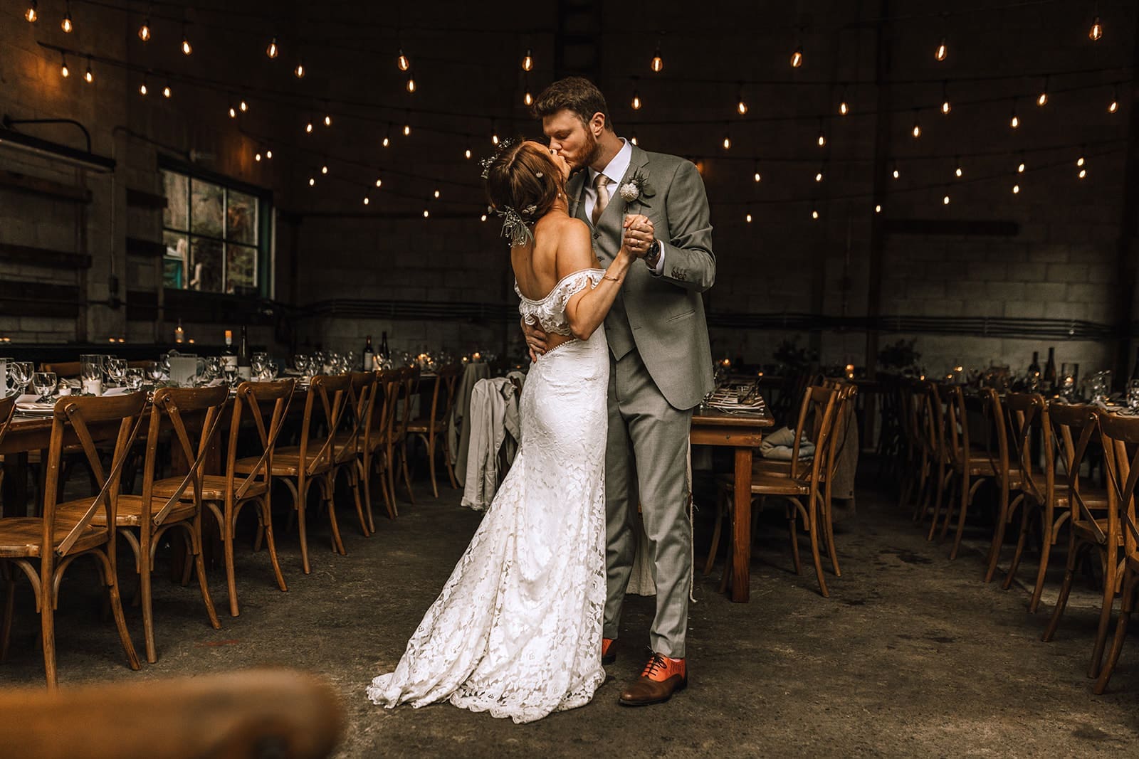 Bride and Groom kissing with string lights overhead in the decorated room with long tables at their Port Renfrew Wedding